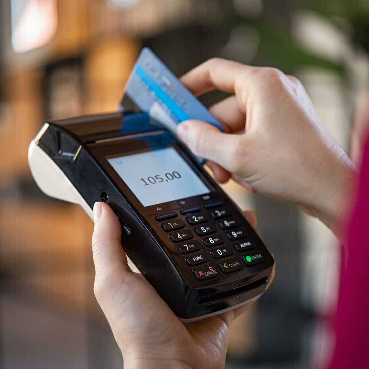 Close up of woman hands making a credit card payment with card reader machine. Credit card swipe through terminal for sale in store. Cashier hand swiping debit card after a purchase.